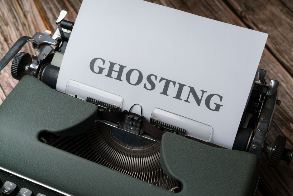 A close-up image of a vintage green typewriter with a sheet of white paper inserted, displaying the word 'GHOSTING' in large, bold, black letters. The typewriter is positioned on a wooden surface, wit