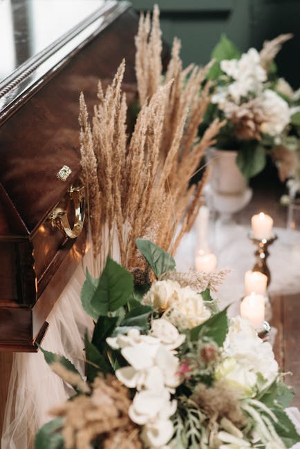 A floral arrangement featuring white and cream-colored flowers, including roses and hydrangeas, complemented by lush green leaves. The bouquet is placed on a surface beside a polished wooden piano, ad